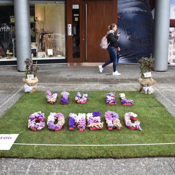 Un quadrat de gespa al terra i sobre un text amb flors que diu: viu el comerç