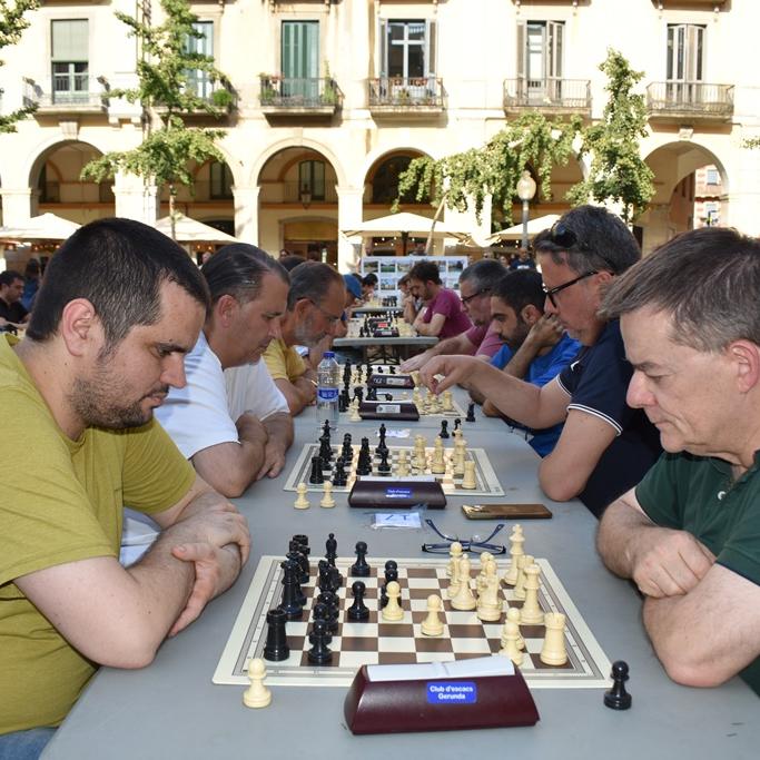 adults jugant a escacs a l'aire lliure en dues fileres, amb dos jugadors en primer pla
