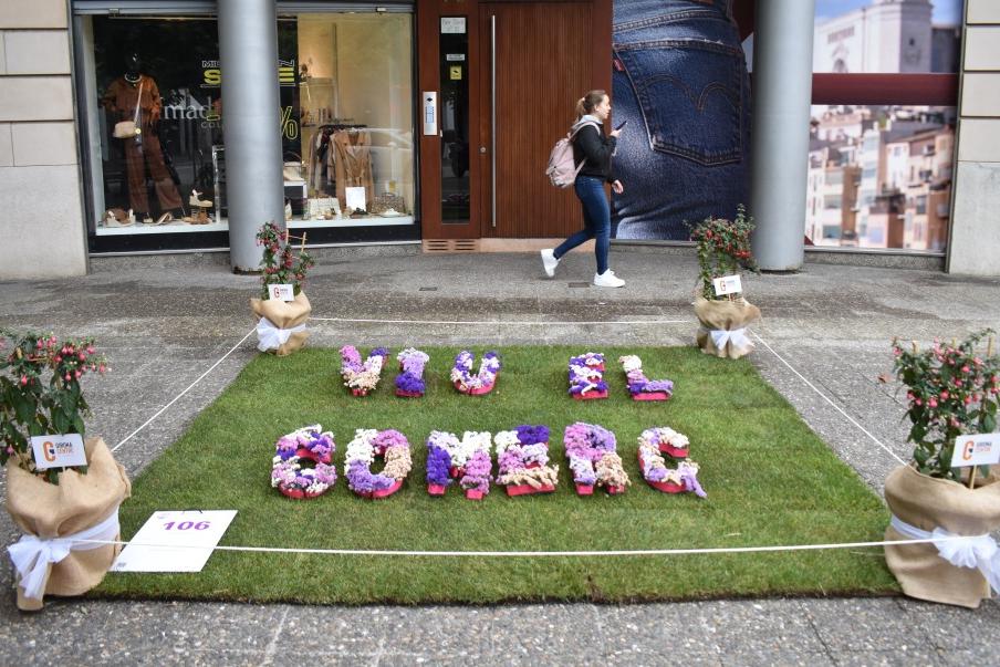Un quadrat de gespa al terra i sobre un text amb flors que diu: viu el comerç