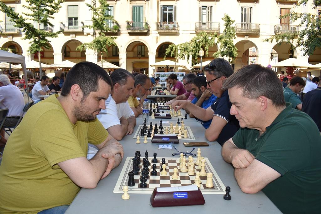 adults jugant a escacs a l'aire lliure en dues fileres, amb dos jugadors en primer pla