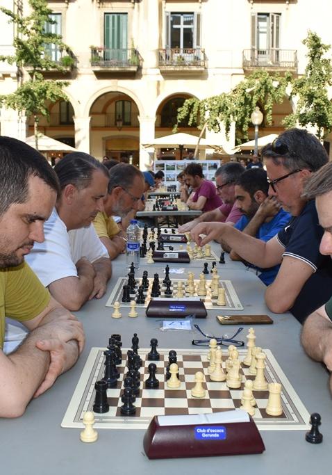 adults jugant a escacs a l'aire lliure en dues fileres, amb dos jugadors en primer pla